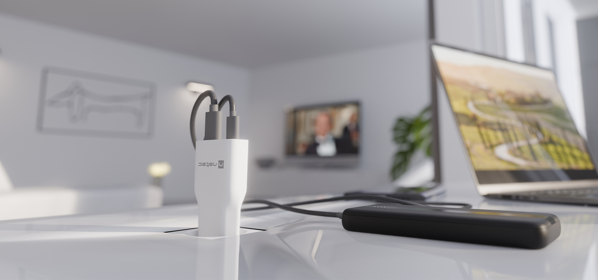 Kompaktowa ładowarka z dwoma kablami połączeniowymi, umieszczona na biurku obok laptopa i telewizora.