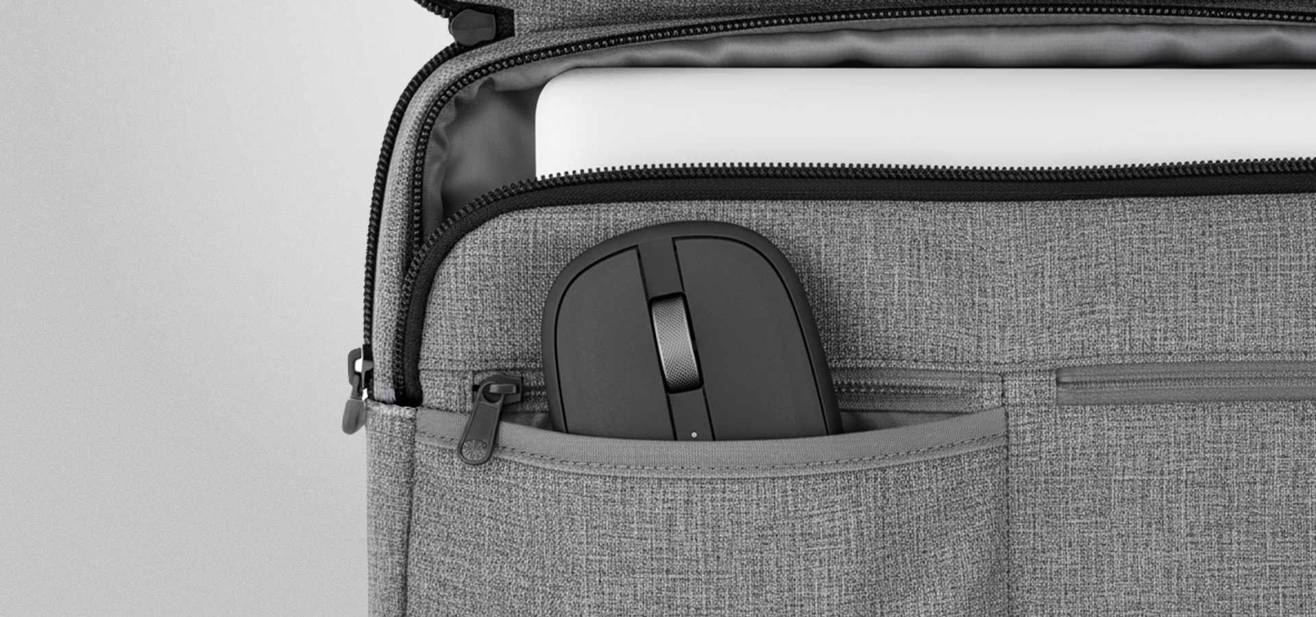 Mysz bezprzewodowa przechowywana w szarej kieszeni torby obok laptopa