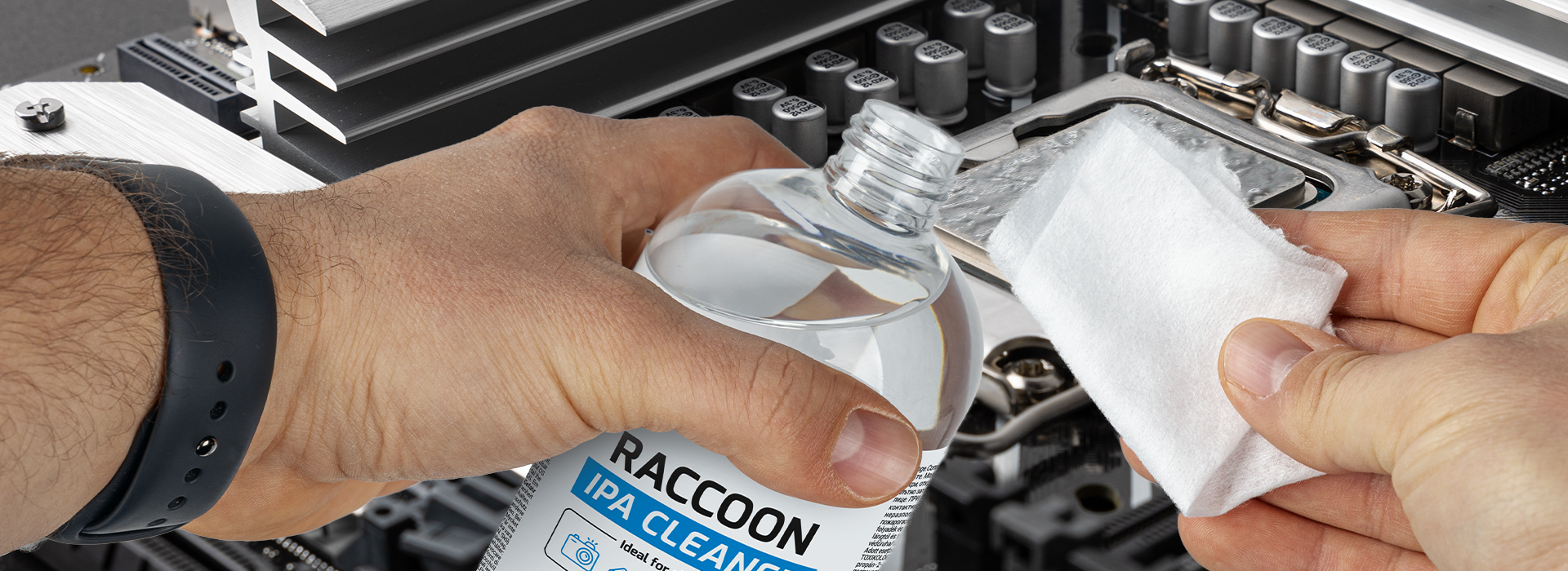 A person holding a bottle of cleaning solution and a cloth near electronic components.