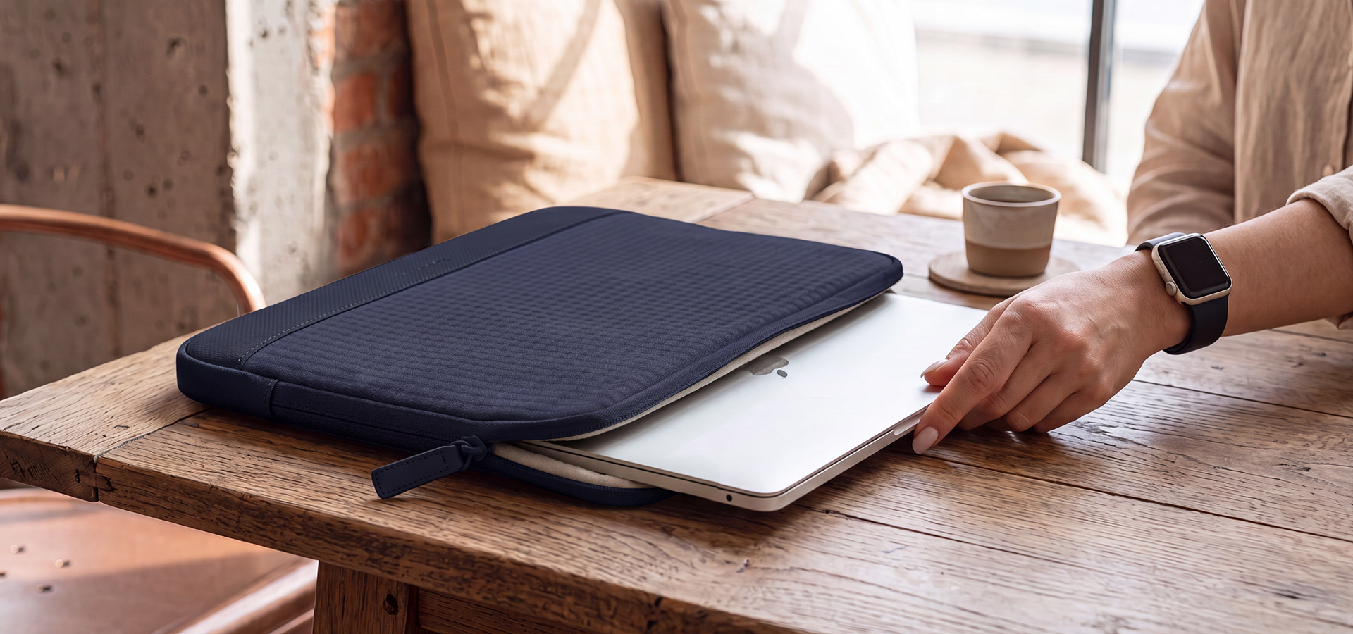 Laptop jest wkładany do ciemnej torby na drewnianym stole obok filiżanki kawy.