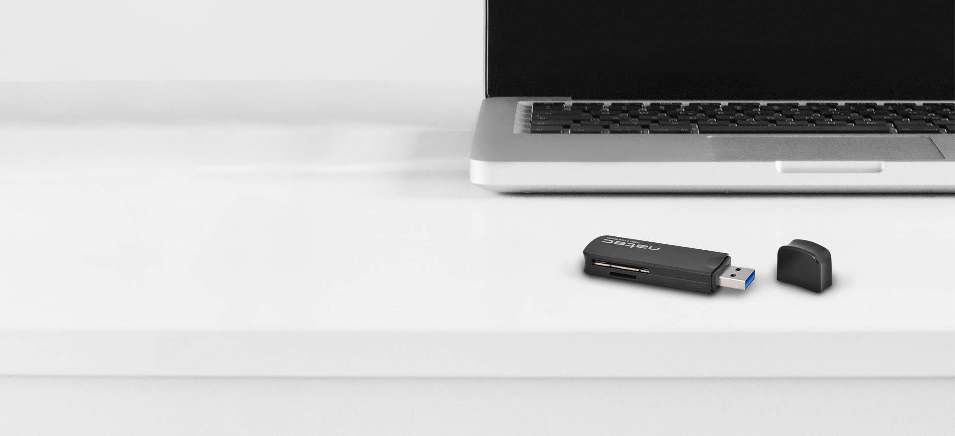 Card reader for SD and micro SD cards, with a protective cap, placed next to a laptop