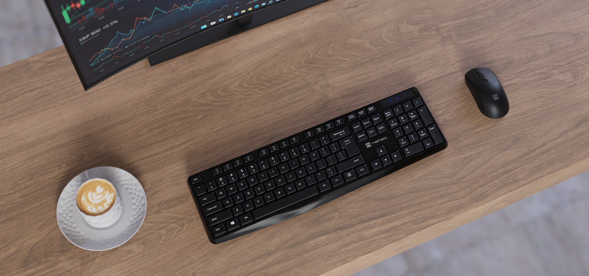 Computer keyboard and mouse on a wooden desk next to a cup of coffee and a monitor.