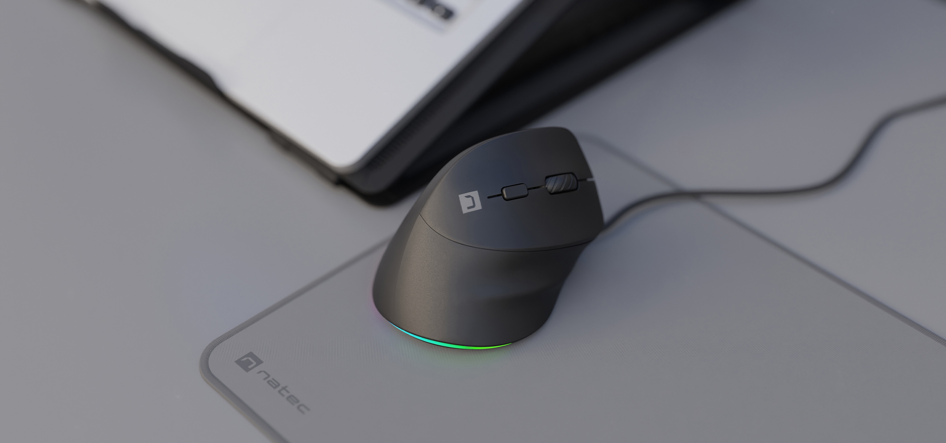 A sleek computer mouse with a connection cable and a glowing light on a mouse pad.