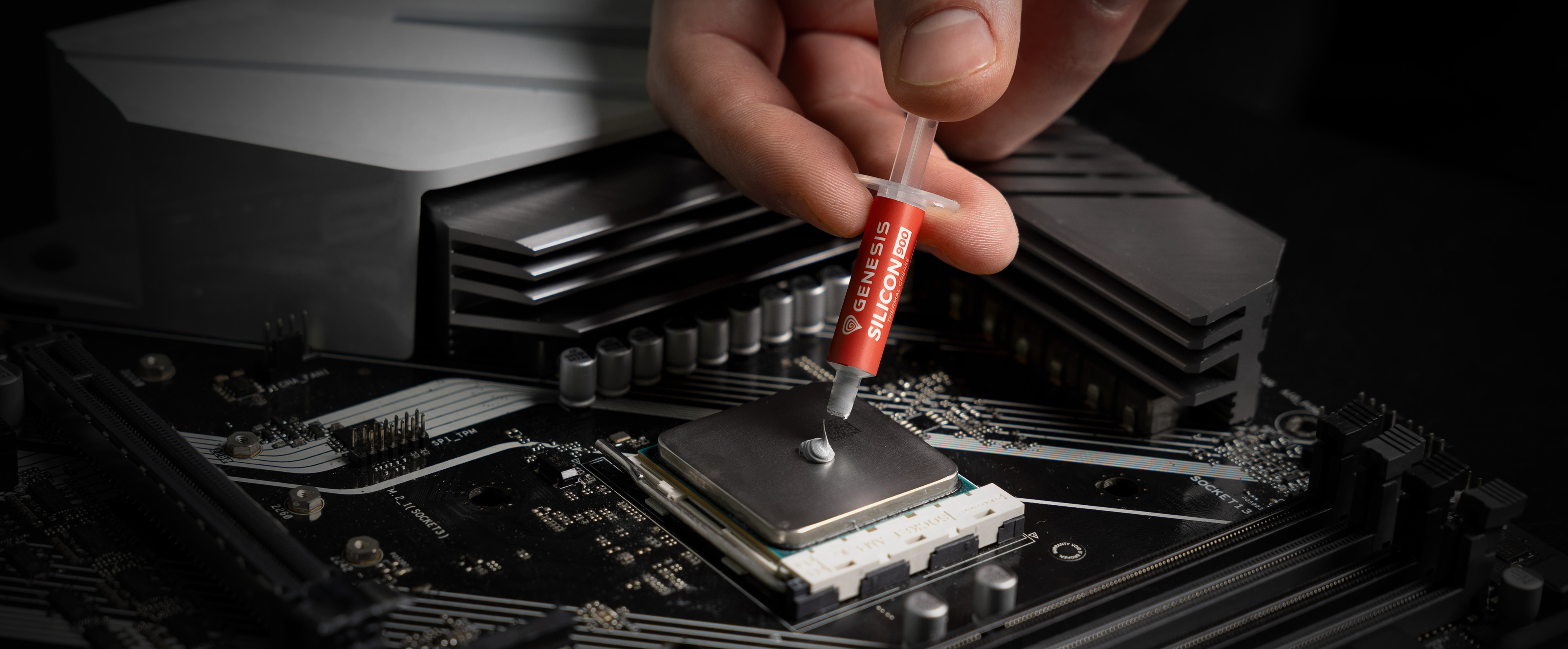 Handauftragen von Wärmeleitpaste auf eine CPU auf einem Motherboard, mit einer eleganten Computerkühlkomponente im Hintergrund