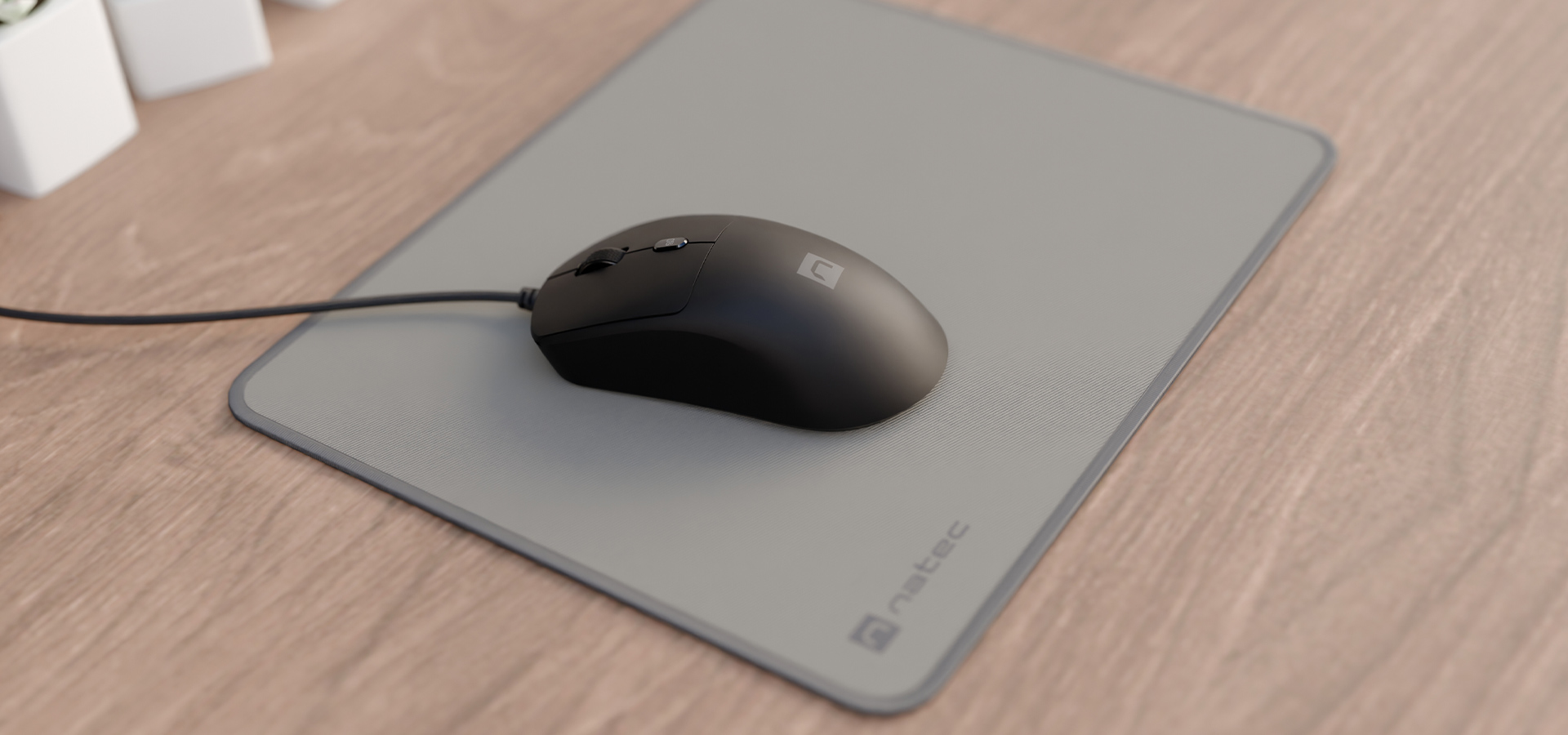 Czarna mysz przewodowa na szarym podkładce na drewnianym biurku.