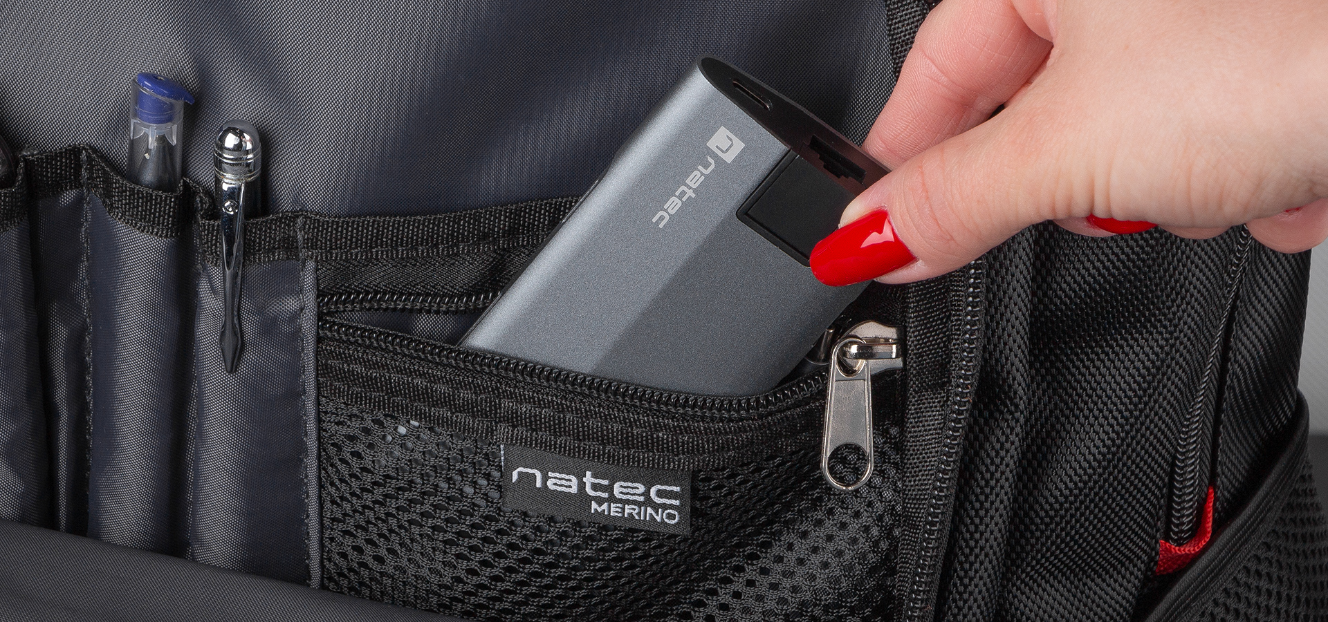 Ręka umieszczająca przenośne urządzenie w kieszeni plecaka z uporządkowanymi przegródkami.