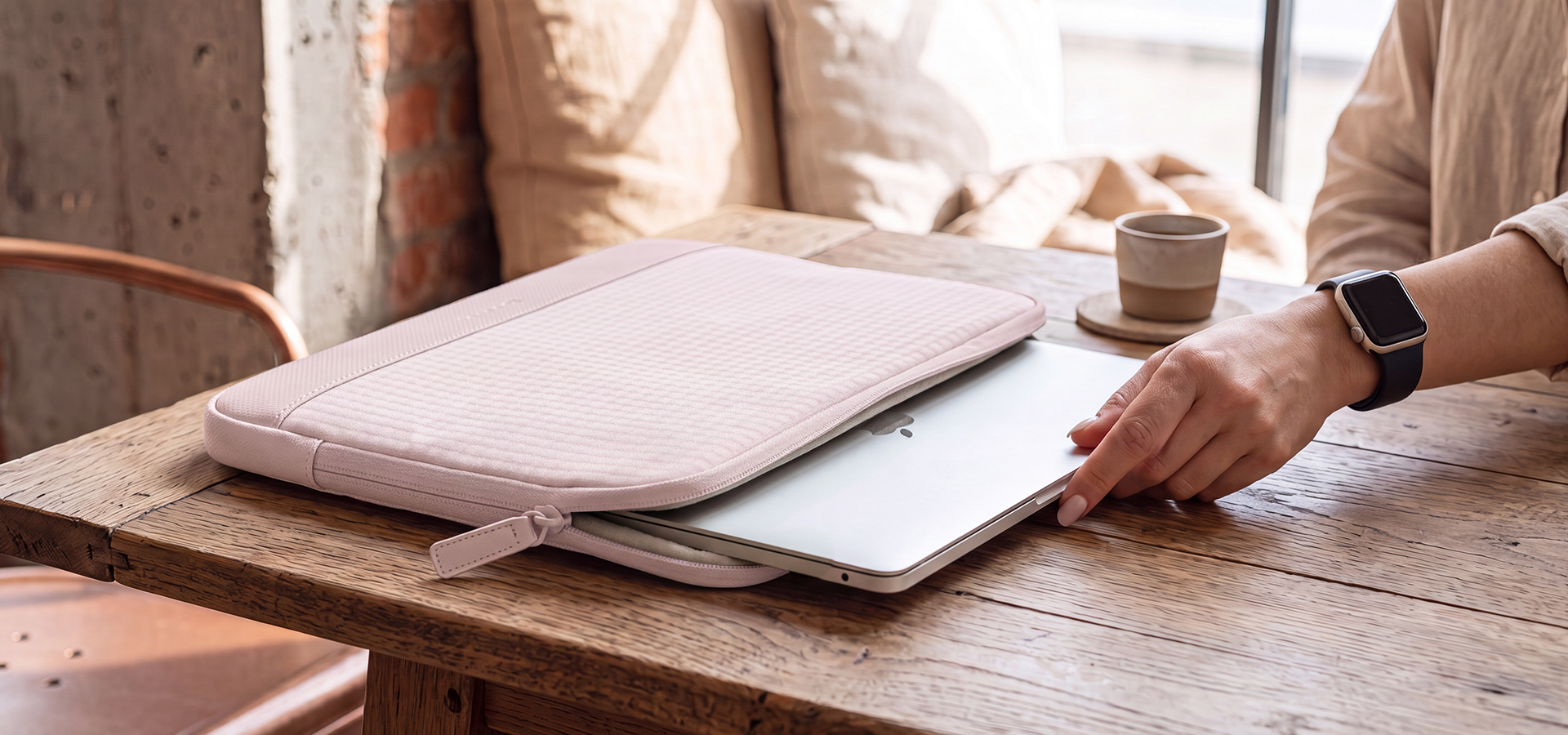 Osoba wkładająca laptopa do jasnoróżowej osłony na drewnianym stole.