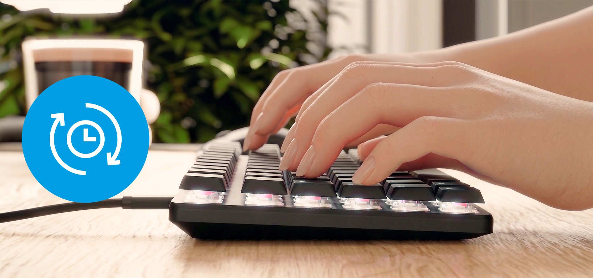 Hands typing on a keyboard with backlit keys sitting on a wooden surface.