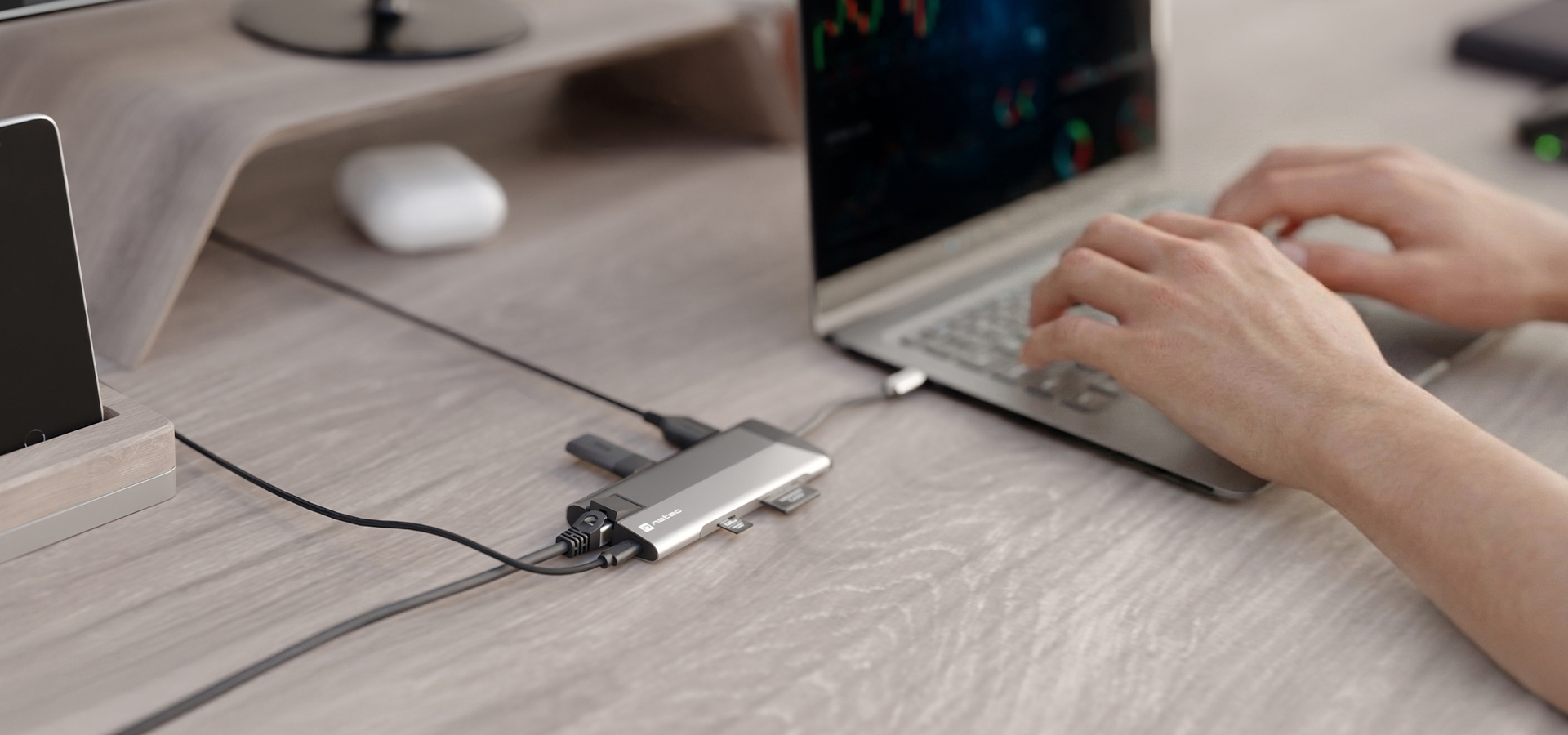 Osoba korzysta z laptopa podłączonego do stacji dokującej na drewnianym stole.