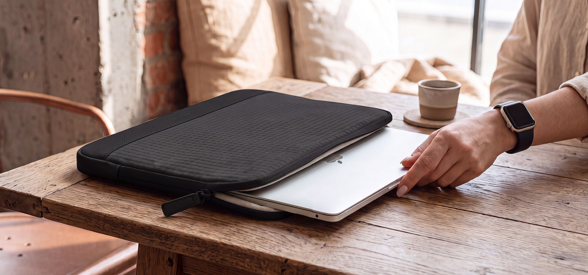 Osoba wkładająca laptopa do czarnej torby na drewnianym stole z filiżanką kawy.