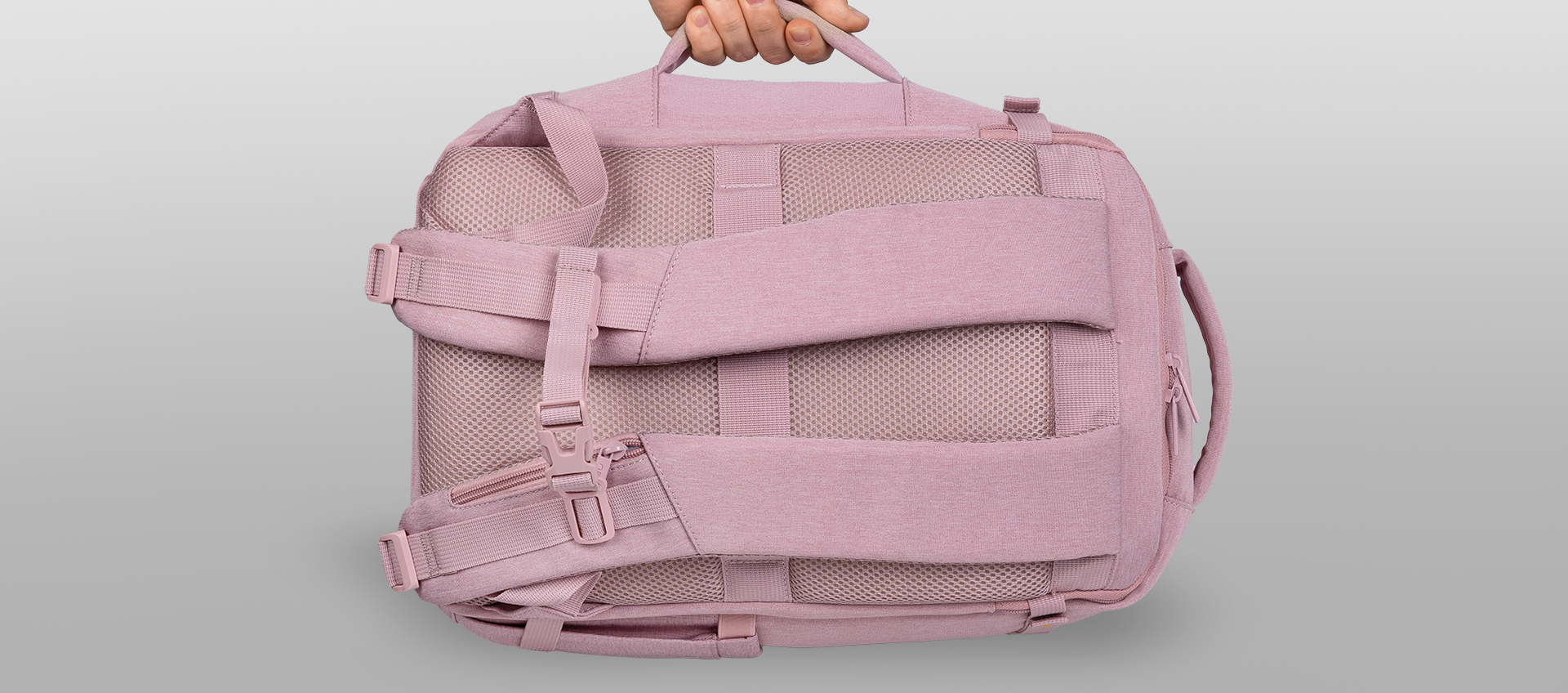 A person holding a pink backpack with straps and mesh material on the side.
