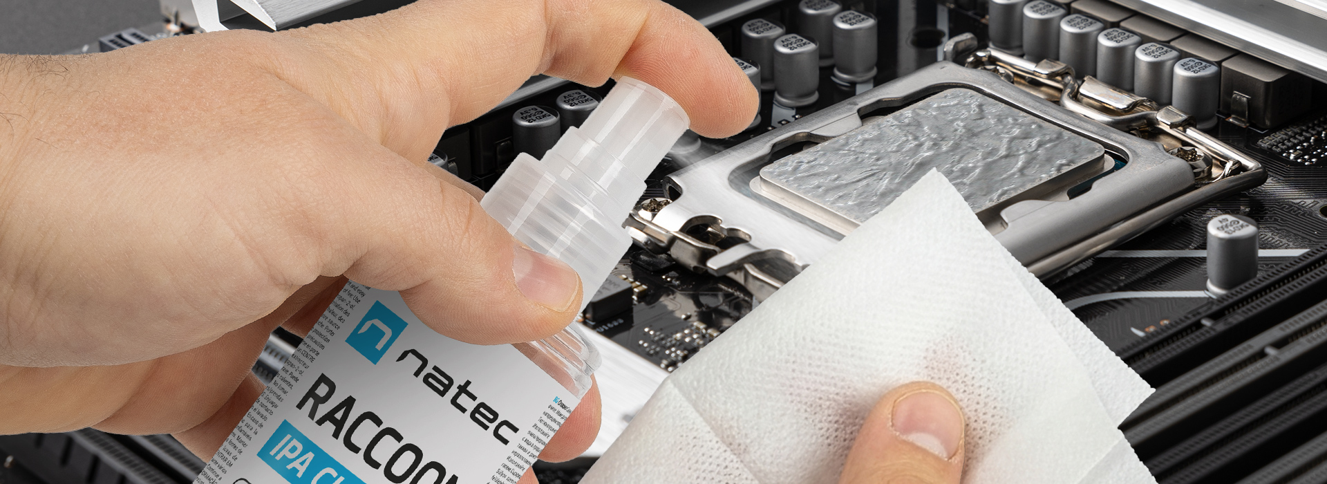 Ręka trzymająca butelkę sprayu obok podzespołu komputera i ściereczki do czyszczenia.
