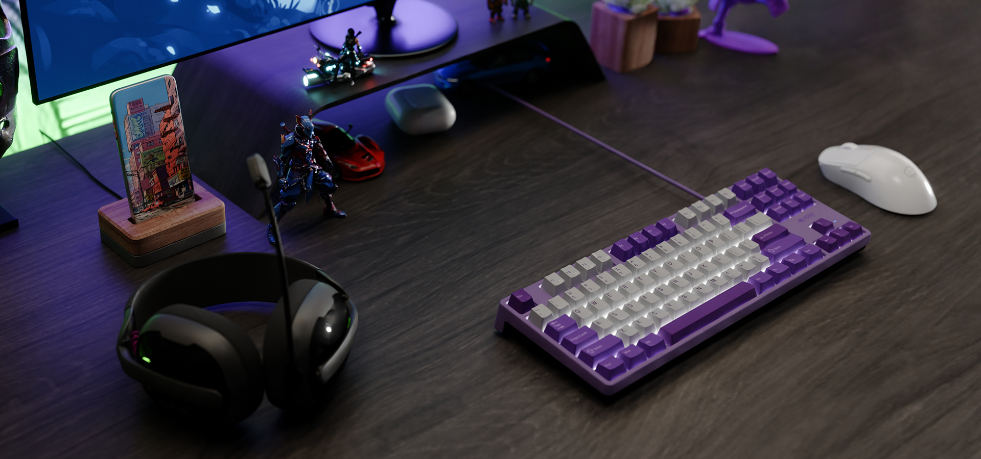 Fioletowa i biała klawiatura, mysz do gier oraz słuchawki na ciemnym biurku z dekoracjami.
