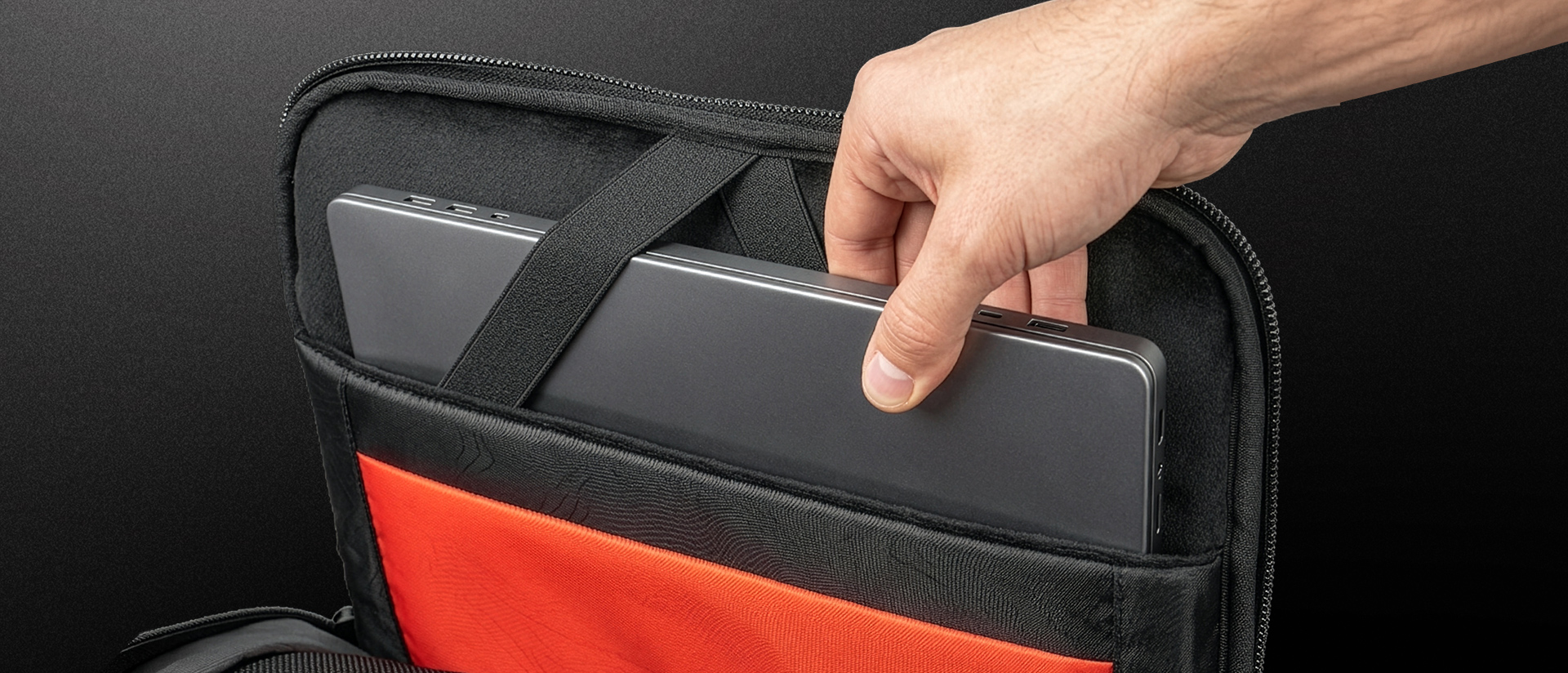 Ręka wyciągająca laptopa z ochronnego etui z pomarańczową kieszenią.