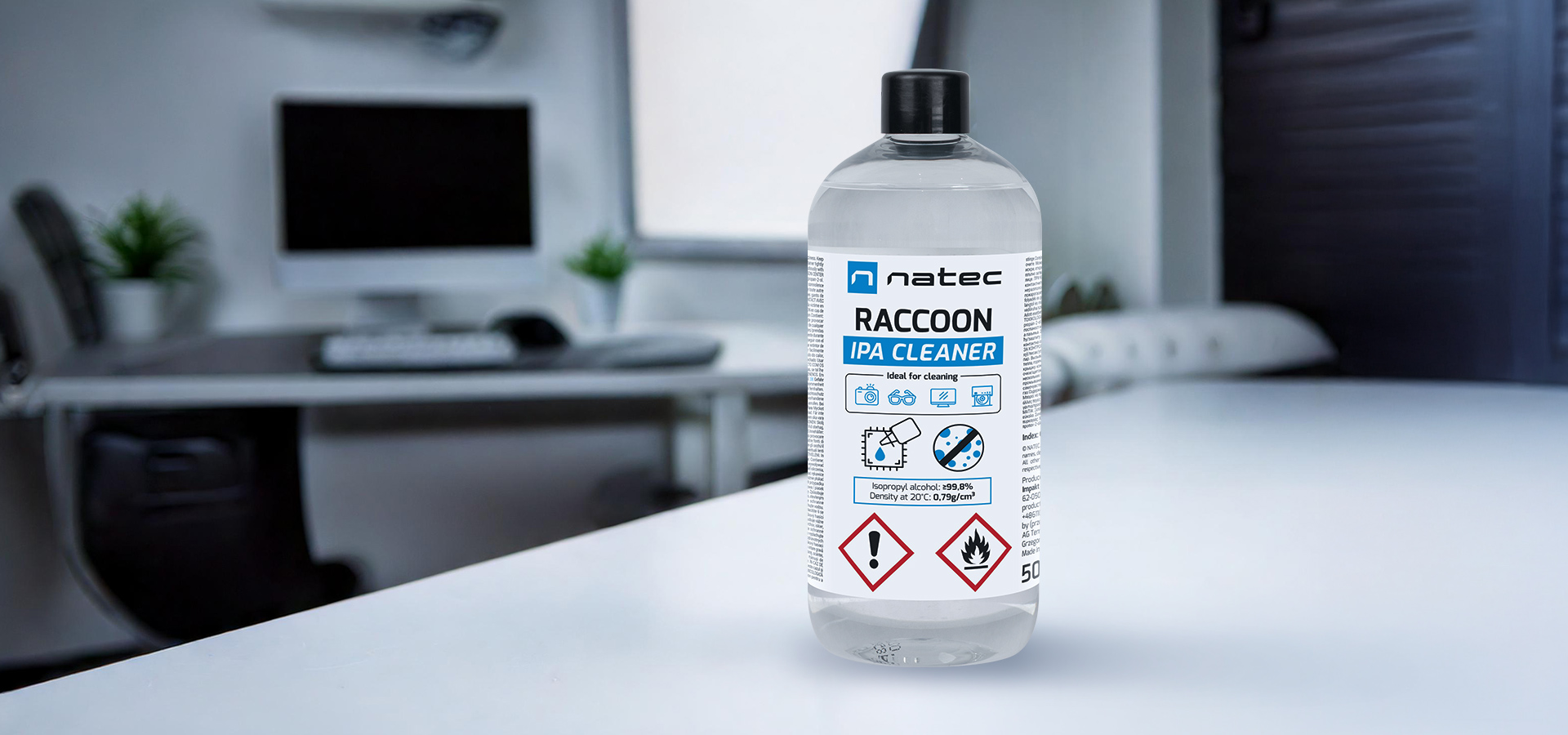 Clear bottle of cleaner on a table in a modern workspace with a computer and plant.