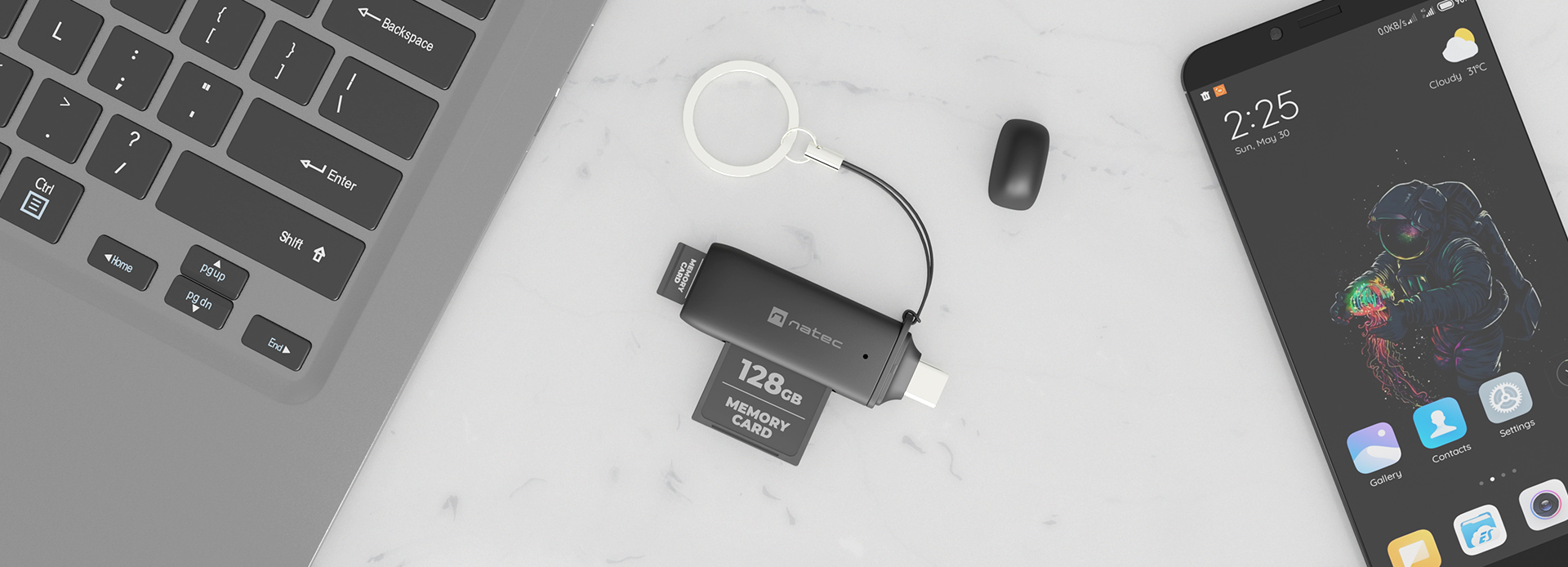 Kompaktowy czarny czytnik kart SD i micro SD, umieszczony na marmurowej powierzchni obok laptopa i smartfona