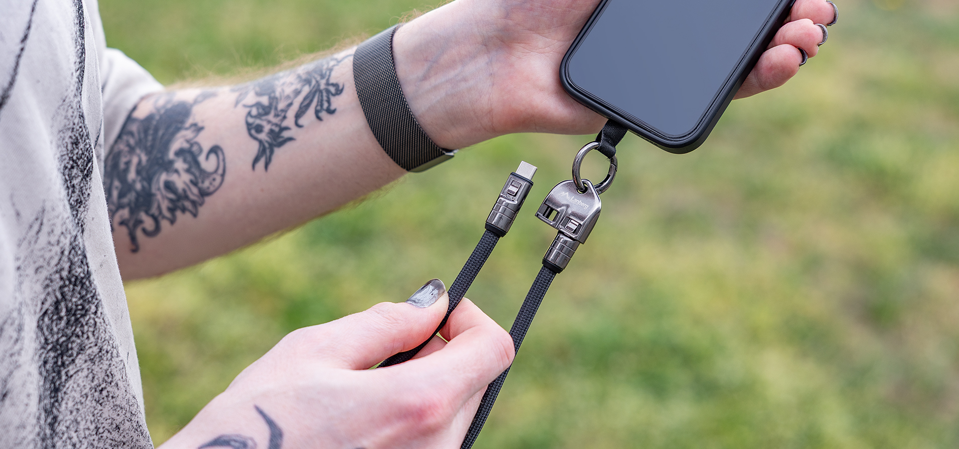 Kabel USB-C z mocowaniem do breloka o długości 0,3 m, trzymany przez osobę w pobliżu smartfona na zewnątrz.