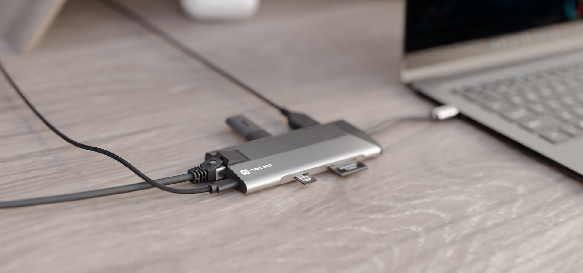 Urządzenie z różnymi portami podłączonymi do laptopa na drewnianym biurku.