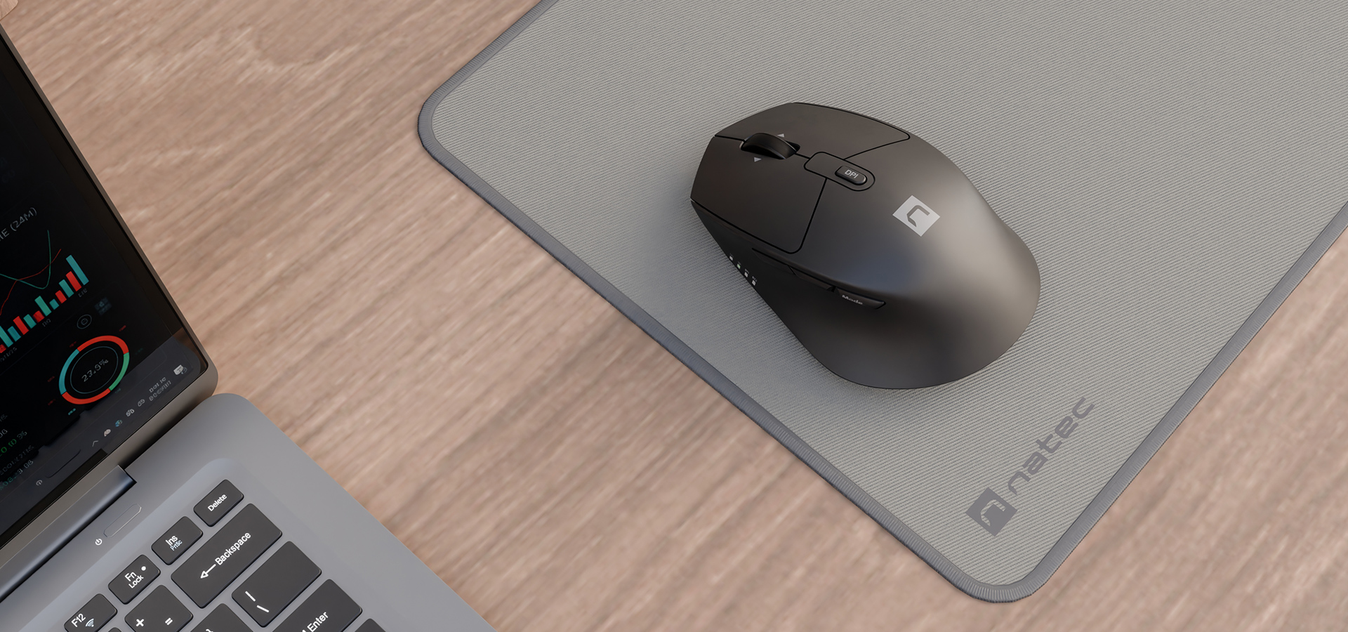 Czarna mysz komputerowa na szarej podkładce obok laptopa i wykresu na ekranie.